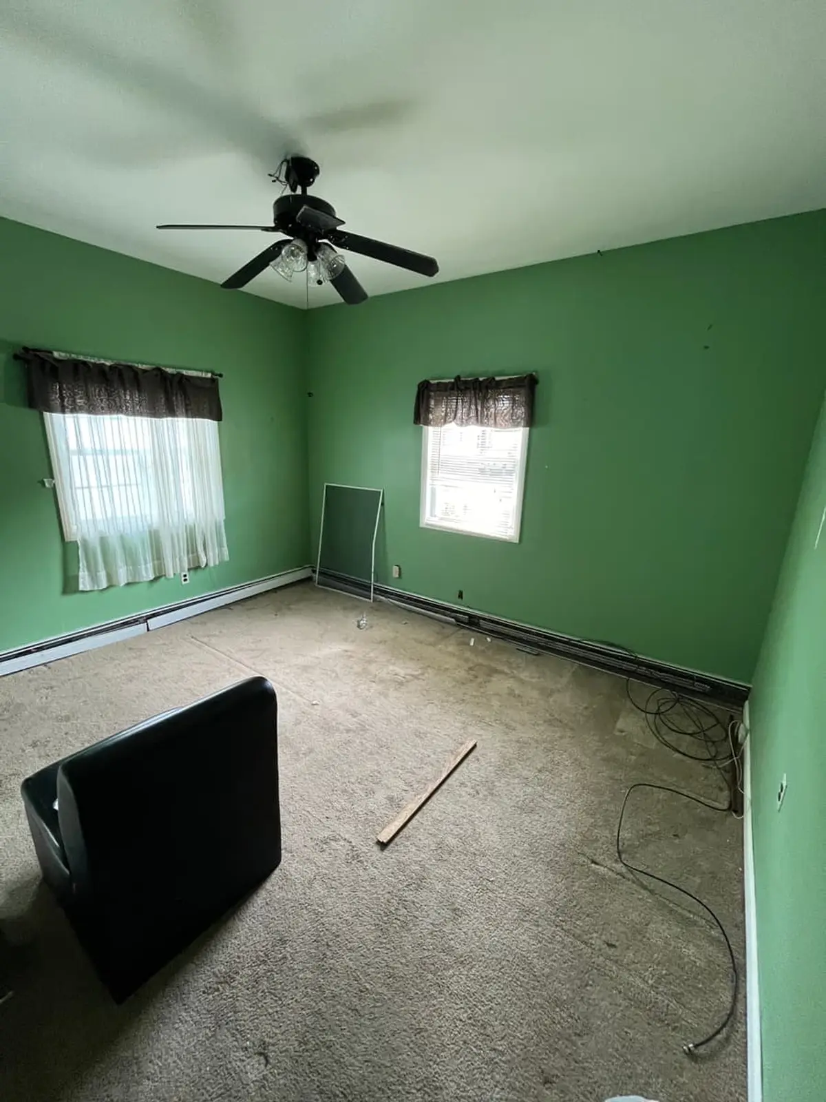 Trying to stop a foreclosure in Ronkonkoma: empty green bedroom with worn carpet and a ceiling fan